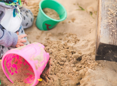 Criança brincando na areia, brinquedos espalhados na areia.