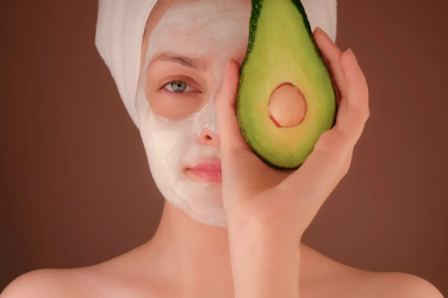 woman putting face mask with half Avocado