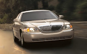 Front 3/4 view of silver 2011 Lincoln Town Car driving with lights on
