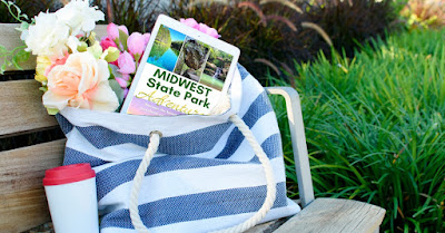 a tablet displaying the ebook Midwest State Park Adventures peeks out of tote bag sitting on a bench in a green park