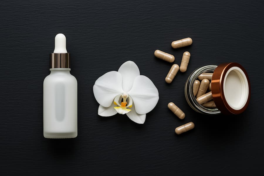Flacone con contagocce, fiore di orchidea bianca e capsule integratori su fondo nero