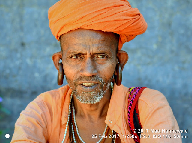 matt hahnewald photography; facing the world; gorakh nath; monk; monastery; bhavnath; bhavnath fair; character; face; earrings; ears; holed; eyes; facial expression; eye contact; stubbly; turban; orange; consent; empathy; rapport; respect; traveling; religious; traditional; cultural; hinduism; festival; event; mela; devotee; pilgrim; junagadh; gujarat; asian; indian; western india; one person; male; elderly; man; picture; photo; face perception; physiognomy; educational; nikon d3100; nikkor af-s 50mm f/1.8g; prime lens; 50mm lens; 4x3 aspect ratio; horizontal orientation; street; portrait; closeup; headshot; full-face view; outdoors; color; posing; authentic; smiling; determined; focused; manly; kanphata; yogi; darshani; gorakhnathi; shaivism; splitted ears