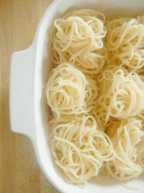 Spaghetti twisted in piles in a white Pyrex baking dish.