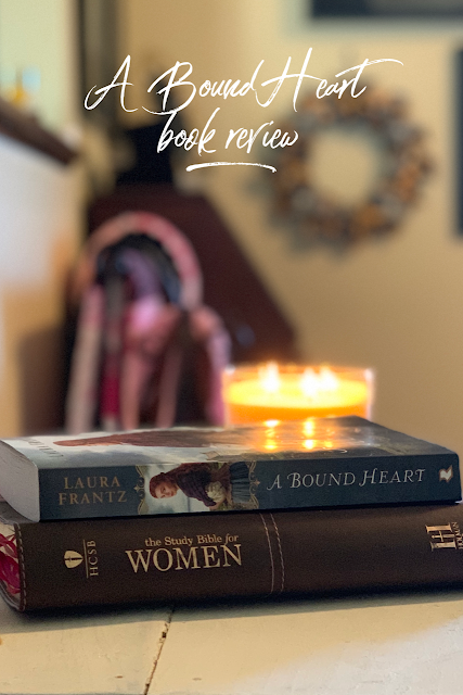 A bible and a book on a white table with a yellow candle burning.