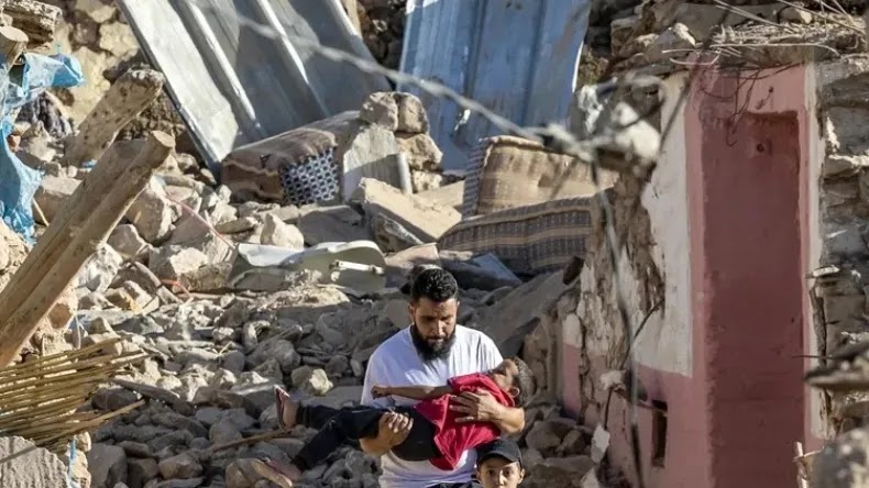 Um homem carrega um menino enquanto ele passa por casas destruídas após um terremoto na vila montanhosa de Tafeghaghte, a sudoeste de Marraquexe, Marrocos | Fadel Senna/AFP