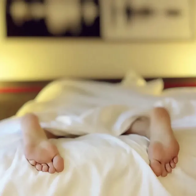 Feet of person lying on stomach on a bed with white sheets and covers.