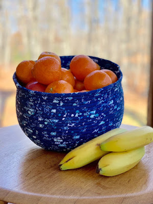 Blue bowl made from fabric-wrapped rope, on a table, filled with fruit