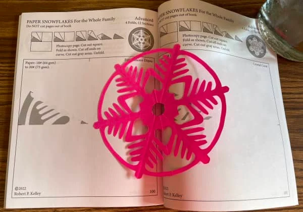 open snowflake book on table with vivid pink papercut snowflake placed on the page