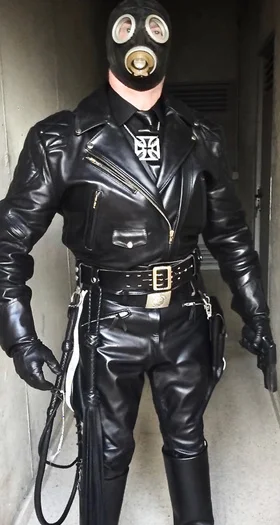A pokey sized leather daddy wearing full black leather gear and a gas mask and carrying gun