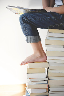 A child sat on a pile of books, reading a book.