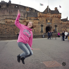 awayfromblue Instagram | tourist hoodie jumping pic at Edinburgh castle pink sweater grey jeans ankle boots