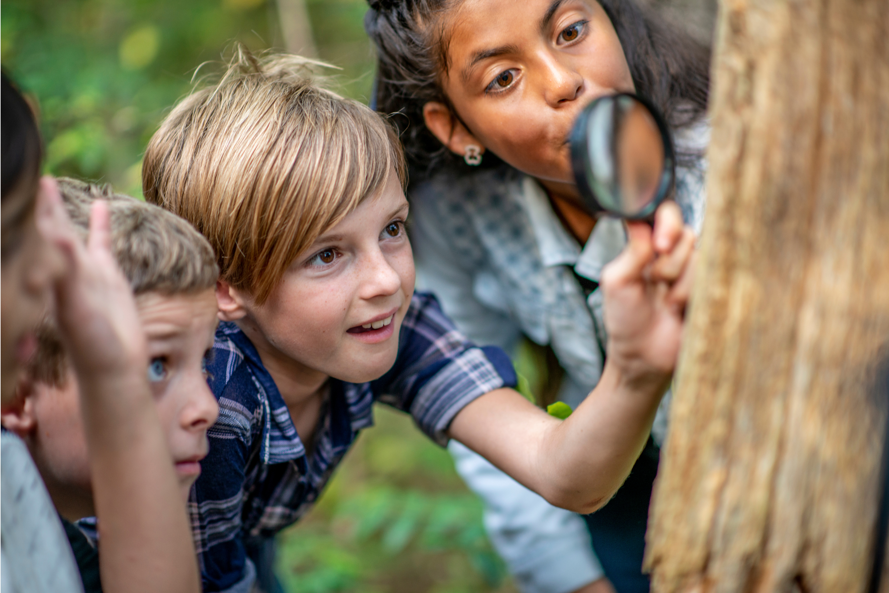 Elementary students gather around a magnifying glass as they explore the world through their imagination