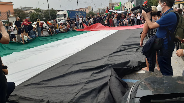 foto di una manifestazione della Palestina: i manifestanti espongono una gigantesca bandiera palestinese