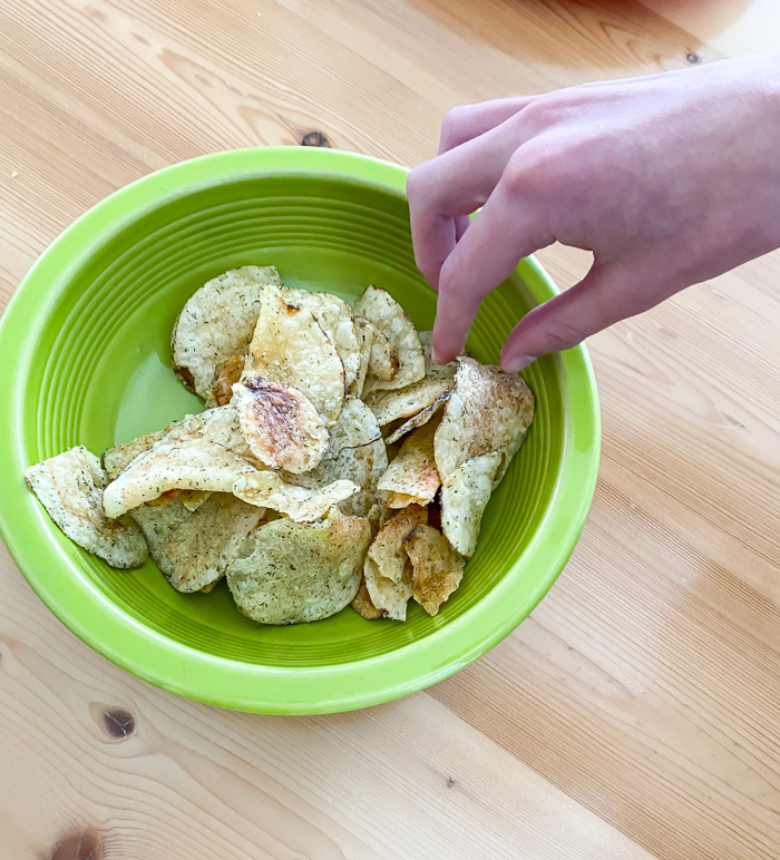 Trader Joe's Dill Pickle Potato Chips in green bowl with hand