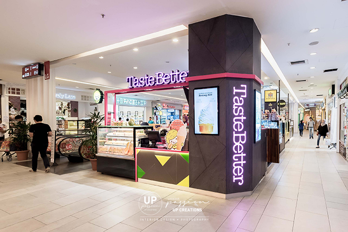 taste better empire subang kiosk column wrapped in dark grey stone texture and wood texture laminate with TV menu and striking corporate pink color metal structure for highlight