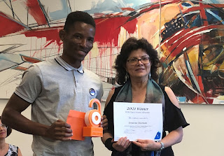 Eminike holds his orange, pad-lock shaped trophy and smiles while Library Director Helen Hooper presents him with the certificate