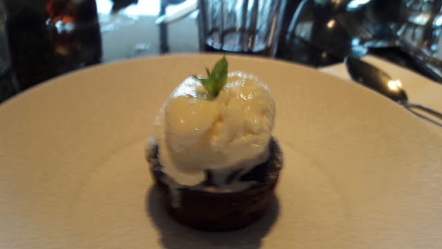 Chocolate pudding, with ice cream on top, with a sprig of mint on a white plate, but out of focus