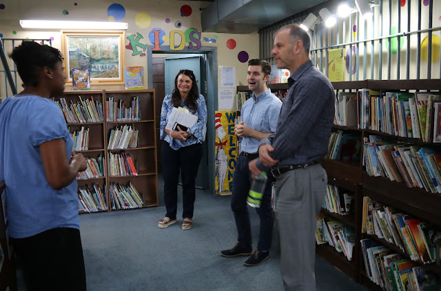 Two men and two women stand in a library talking. This library used to be a jail and still has the bars.