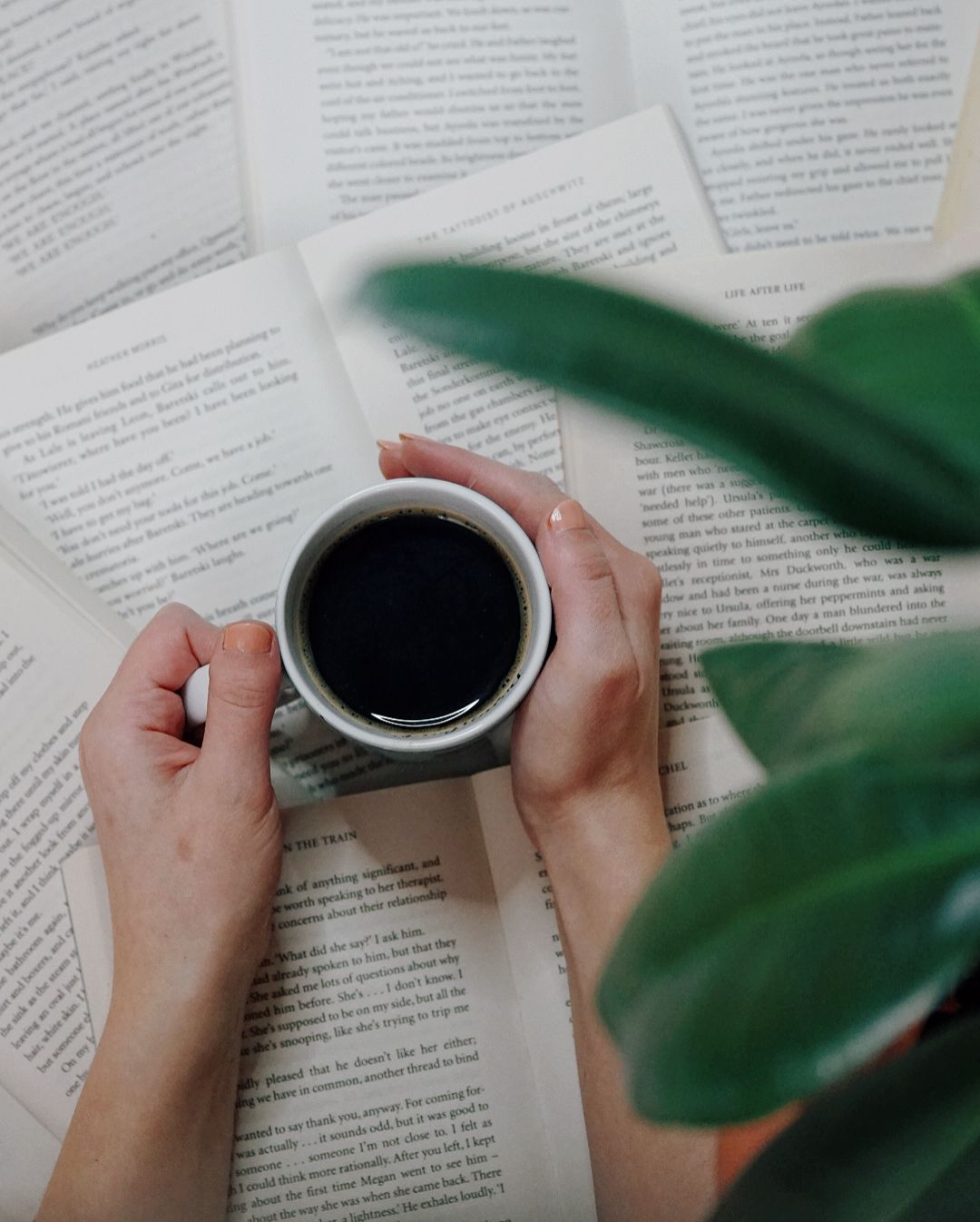 books are laid out open on the floor, hands are holding a cup of coffee out on top of them