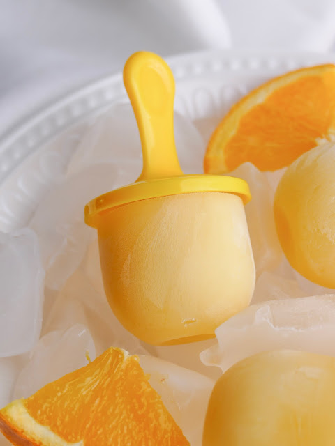 Creamy Orange Popsicles on ice with an orange slice on the side.