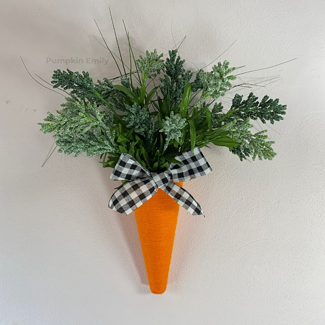 A orange and green carrot wreath door hanger with a bow.