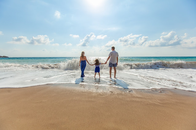 Familia formada por mamá, papá e hija a la orilla de la playa.