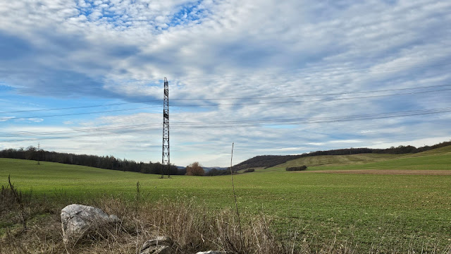 A lone pylon stands in a field connected by wires on either side.