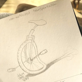 A photograph of a pencil drawing in a sketchbook. The drawing is of a unicycle, in cartoon style, moving quickly from right to left across the page. It has no rider.