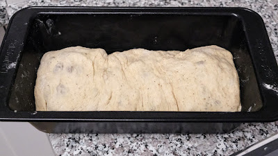 Sultana bread dough in a black loaf tin