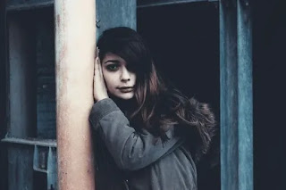 An image of a girl standing by the support of the pillar wearing a black jacket- sad girl dp