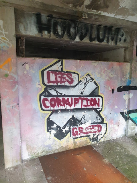 Semi-professional graffiti in the basement stating "lies, corruption, greed"