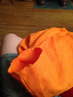 An open tube in a mass of bright-orange fabric, with a partially finished seam running around the top of the tube.