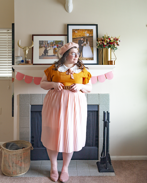 An outfit consisting of a pastel pink beret, a white oversized ruffle peter pan collar under a mustard yellow dress with flounce sleeves under a pastel pink pleated midi skirt and dusty pink pointed toe mules.