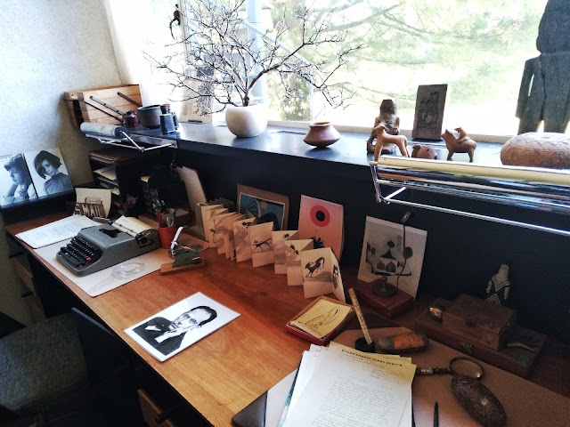 A wider view of the previously described desk, this view emphasizing the ancient artwork on the window sill above the desk, along with a portrait of Walter Gropius laying on the desk.