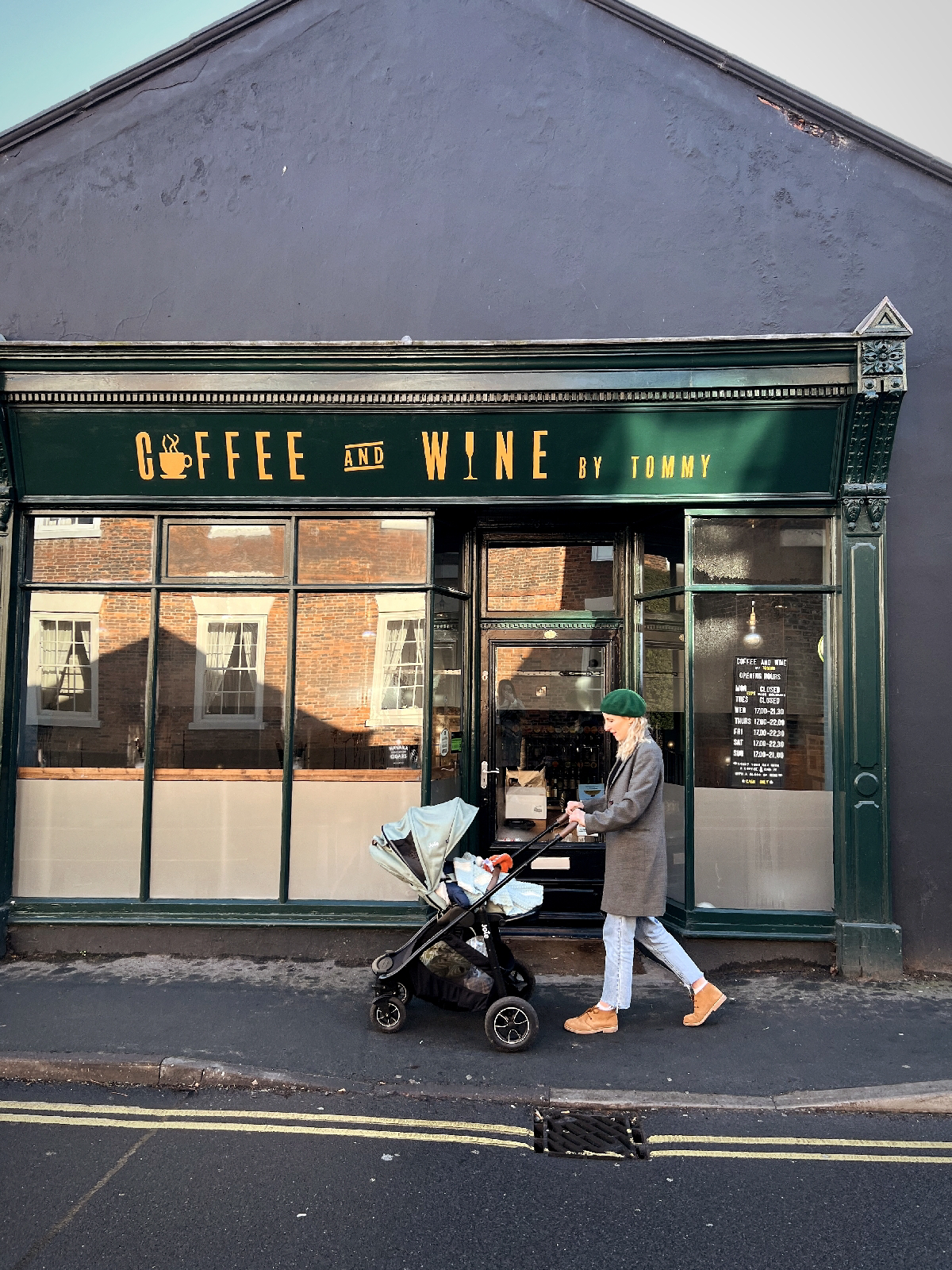 Amy is pushing a pram outside a green fronted shop called 'Coffee and Wine'