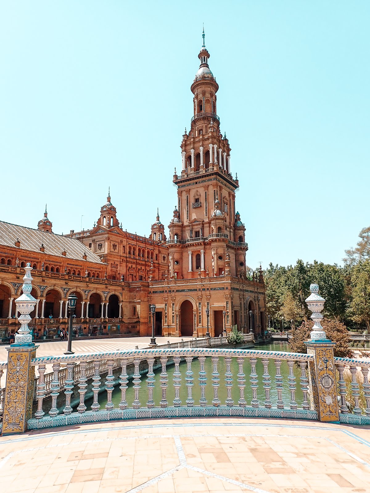 l'une des colonnes de la plaza de espana de séville en arrière plan avec au premier plan l'un des ponts de la place de couleur jaune blanche et bleue