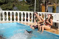 Pareja riendo sentada al borde de la piscina con los pies dentro del agua.