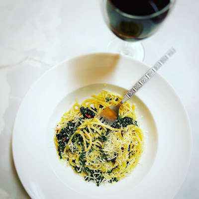 Spaghetti with kale on a dish with a fork and a glass of red wine