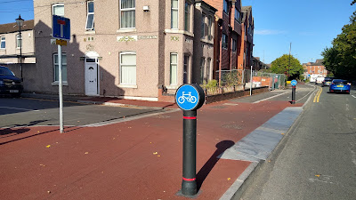 A side road junction which has a raised area surfaced red over which a shared pavement and cycle track crosses.