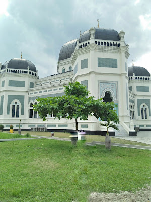  Masjid Raya AL- Mashun Medan Tempat wisata Religi yang kini berusia 113  Tahun  Medan seperti tak ada habisnya untuk ditelusuri, kamu yang suka wisata sejarah atau heritage seperti Saya pasti tak akan melewatkan tempat yang satu ini, yah Masjid Raya Al- Mashun Medan meninggalkan banyak sejarah di dalamnya. Masjid yang berlokasi tak jauh dari pusat kota Medan ini terletak di Jalan Sisingamangaraja No.61Medan Maimun. Pembangunan Masjid Al- Mashun sendiri dimulai pada tanggal 21 Agustus 1906 (1 Rajab 1324 H) oleh Sultan Ma’mun Al- Rasyid Perkasa Alam yakni pemimpin Kesultanan Deli pada masa itu. Dan secara keseluruhan pembangunan selesai pada tanggal 10 september 1909 yang artinya waktu pembangunan yang dibutuhkan adalah 3 tahun lebih. Dilansir dari Simas.kemenag.go.id Masjid yang Luas bangunannya sampai 5.000 m2 menelan biaya pembangunan mencapai satu juta Gulden. Kemudian Masjid ini juga ini memiliki daya tampung hingga 1.500 jamaah. Masjid yang dibangun di atas lahan seluas 18.000 kini sudah memasuki usia satu abad lebih, tepatnya berumur113 Tahun.  Menurut sejarahnya, Sultan Ma’mun Al-Rasyid memang sengaja membangun Masjid ini dengan megah, karena menurut prinsip nya hal itu lebih utama ketimbang kemegahan Istananya sendiri, yakni Istana Maimun yang berjarak 200m dari Masjid. Kemudian, pembangunan Masjid ini ditanggung sendiri oleh Sultan Ma’mun Al- Rasyid, namun konon katanya Tjong A Fie, tokoh saudagar kaya dari etnis Tionghoa ini pun turut berkontribusi dalam pendanaan pembangunan Masjid Raya ini. Pada mulanya arsitek yang merancang bangunan Masjid Raya ini merupakan Van Erp arsitek asal Belanda yang sebelumnya juga merancang Istana Maimun, namun kemudian prosesnya dikerjakan oleh JA Tingdeman. Alasanya karena ketika itu Van Erp dipanggil ke pulau Jawa oleh pemerintah Hindia Belanda untuk bergabung dalam proses restorasi candi Borobudur di Jawa Tengah. Kemudian JA Tingdeman merancang masjid ini dengan denah simetris segi delapan dalam corak bangunan campuran Maroko, Eropa dan Melayu serta Timur Tengah.  Pada bangunan masjid dibagi atas beberapa ruang utama, tempat wudhu, gerbang masuk dan menara. Ruang utama, tempat sholat berbentuk segi delapan tidak sama sisi. Pada sisi berhadapan lebih kecil, terdapat beranda yakni serambi kecil yang menempek menjorok keluar. Di bagian dalam masjid terdapat pilar utama berdiameter 0.60 m yang menjulang tinggi. Masjid Raya Al- Mashun didominasi warna putih, di samping hijau pada sekitar bagian pintu-pintu dan warna hitam pada kubahnya. Pilar-pilar yang terdapat pada setiap sisi bangunan untama mengambil corak khas Cordoba dan spanyol, terutama dengan lekung bagian atas yang berbentuk setengah lingkaran. Untuk membangun Masjid Raya Al- Mashun banyak dekorasi yang diimpor dari mancanegara seperti marmer dari Italia, kaca patri asal Cina, dan lampu gantung dari Prancis. Seriap ornamen dihiasi dengan ukiran-ukiran indah bermatif floral atau geometris. Keindahan Masjid Raya Al-Mashun dan Istana Maimun menandakan tingginya peradaban Kesultanan Deli, sebagai suatu kedaulatan etnis Melayu yang sempat berjaya pada zaman lampau. 