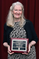 Dr. Coffin smiles and holds her award plaque 