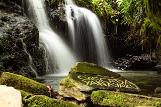 Parte de las impresionantes cascadas Yanayaku, donde el agua cae en forma de cortina, mientras el nombre 'Cascadas Yanayaku' está escrito en una piedra, creando un escenario majestuoso.