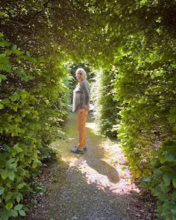a woman standing in a pool of light surrounded by greenery.