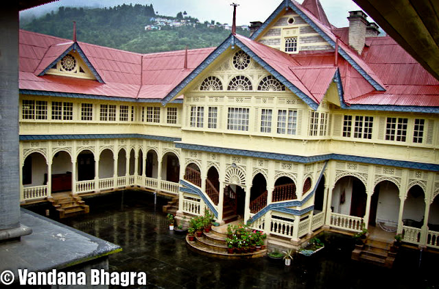 An architectural marvel: Jubbal Palace : By Shimla, Vandana Bhagra : Photo credits: Given by the owners : When we use the phrase “har ghar kuchh kehta hai”, a novel concept adopted by the Himachal government in promoting heritage properties of Shimla town, we often associate them with the Britisher’s rule, rich in history with facts, photographs and antiques dating back to that period. And when we talk about royalty we are equally impressed by the grandeur and imperial finesse with which they once lived in or are still living. One such architectural marvel is the Jubbal Palace, residence of HH Raja Rana Yogendra Chandra and Rani Sudha Kumari, about 92 kms from Shimla taking approximately four hours to reach via Theog, Kotkhai and Khara Patther. The setting is just picture perfect, with River Bishkalti on one side and the Kuper peak as the backdrop. Once described in the Imperial Gazetteer of India as being “built in partially Chinese style, the lower portion consisting of masonry, while the upper half is rined round with wooden galleries capped by overhanging eaves. The Palace is remarkable for the enormous masses of deodar timber used in its construction”. Rightly said, as when you walk through the Durbar Hall or the Indian style baithak your steps are arrested by the massive paneling work done on the ceilings, the intricate woodwork, carved bordered facades, Persian carpets and antiques all around the rooms are enough to give you a royal feel. The Durbar Hall has these carved jharokhas on the upper floor, then used by women to watch the proceedings below or the royal functions which were held during those days, were initially built by a women craftsmen from Chaupal and even till date they remain as pristine as ever. As royalty would have it, there were different drawing rooms for both men and women and as Raja Yogendra Chandra adds, “even Raja and Rni had separate bedrooms connected with a spiral staircase”. Family heirlooms which can be seen are quivers and arrows, family portraits, pieces of art and ivory ilaid peacock chairs. The stunning display of ancient artilleries ranging from cannons, swords to muskets and shield will just tickle your senses and give you a feeling of being a warrior. The fireplaces add an old charm to the Palace which has a collection of Kangra paintings on the Radha Krishna theme hung over them.  The old structure was brought down in 1935 and what stands now is a mix of Gothic, Art Deco and local architecture. An interesting anecdote Sudha Kumari states “It was decided that a new Capital would be built for administrative purposes, which would have a new Palace, a tehsil, a prison and an armoury and Old Jubbal would only be used for religious functions and on these grounds a pujan was performed during which as a ritual a chicken was sacrificed. The place where this chicken would land would be earmarked as the new location of the Palace. The bird landed on a small hill formerly known as Deora, now Jubbal, where construction began”. Despite the fact that a French architect was hired to dothe initial structure but Rani Sudha, soon after marriage in 1960, involved herself with the construction of the Palace and personally saw to it that the esthetics of the place was maintained. The modern wing of the Palace exhibits an inquisitive blend of Indo and European styles. Even after the Sheesh Mahal and three other buildings in the Palace complex were burnt down on 29th October 1969, she ensured that same style was adopted while reconstructing the building. The Sheesh Mahal was adorned with large framed mirrors with all modern facilities, the construction of which was started by Raja Sir Bhagat Chandra of Jubbal in 1911 and was completed in 1918.  Whereas the present Palace was built by his son Raja Digvijai Chandra and the construction was started in 1935. Raja Yogendra Chandra, adds “construction of buildings, prior to the making of Sheeh Mahal during those days, was done without using any iron nails as only wooden pegs were used to hold thestructure. Layers were made of stone and wooden beams whih held the structure firmly and resistant to earthquakes or tremors. While undertaking construction of the new sections these concepts were kept in mind”. The entrance of the Palace opens into the central courtyard where a temple stands tall with a Pagoda style roof and a unique feature as lead has been used in its construction. Nestled behind the temple tower is the oldest wing of the Palace built in Pahari-style with alternate courses of dressed stone and wooden beams. There are numerous numbers of bedrooms with attached bathrooms, built around the courtyard, furnished with Persian carpets, amazing accessories and beautifully carved furniture. The umpteen number of artifacts and family treasures discovered in the old wing of the Palace have been restored and displayed all over the Palace by Sudha, who spends nearly four months in a year at Jubbal.  Rani Sudha says, “a section of the property was opened to guests but since the courtyard was common and our private quarters were in the same area we felt that ur privacy was being disturbed. In spite of the fact that we were overbooked, we decided to close the property for guests just after a month. Communication too was a huge problem due to bad road conditions”. Admiringly Yogendra Chandra says, that the upkeep and maintenance of the Palace is credited to my wife and son who look after the place as its fresh paintwork, polished woodwork round the clock, sparkling windowpanes and glistering balconies are a thing to fathom. The upcoming library section is a welcome addition to their Palace as it holds a treasure of books collected over a period of time. Rani Sudha reminisces and ends on a note on how Jubbal earned its name, “one day a person was seen digging and planting seeds, and second day a joob (evergreen grass) came up, or dhub, used on auspicious occasions, and he called it as a good omen saying that there would be everlasting greenery and prosperity, and the Raja, who was then staying in Raika, near Hatkoti, should build his Palace here. Hence, this place arned its name as Jubbal”.
