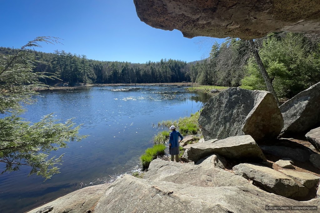 Hiker looking out over a pond, with large boulders in the foreground, both below and above.