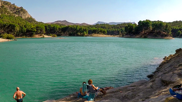 Un lago interior con montañas y abundante vegetación al fondo un orillas rocosas que se asemejan a playas costeras.