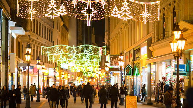 shoppers walk through an outdoor mall decorated with holiday lights