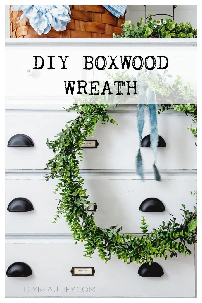 faux boxwood wreath hanging on front of white dresser, blue velvet ribbon