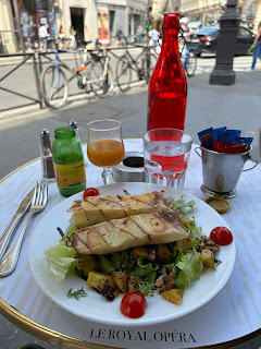 My lovely lunch at the Royal Opera Café - a salad with roasted potatoes, tomatoes, and walnuts, topped with goat cheese crepes.  Behind my plate is a red wine bottle filled with water and a glass of apricot juice.  Two bicycles are parked by the street beyond the table.