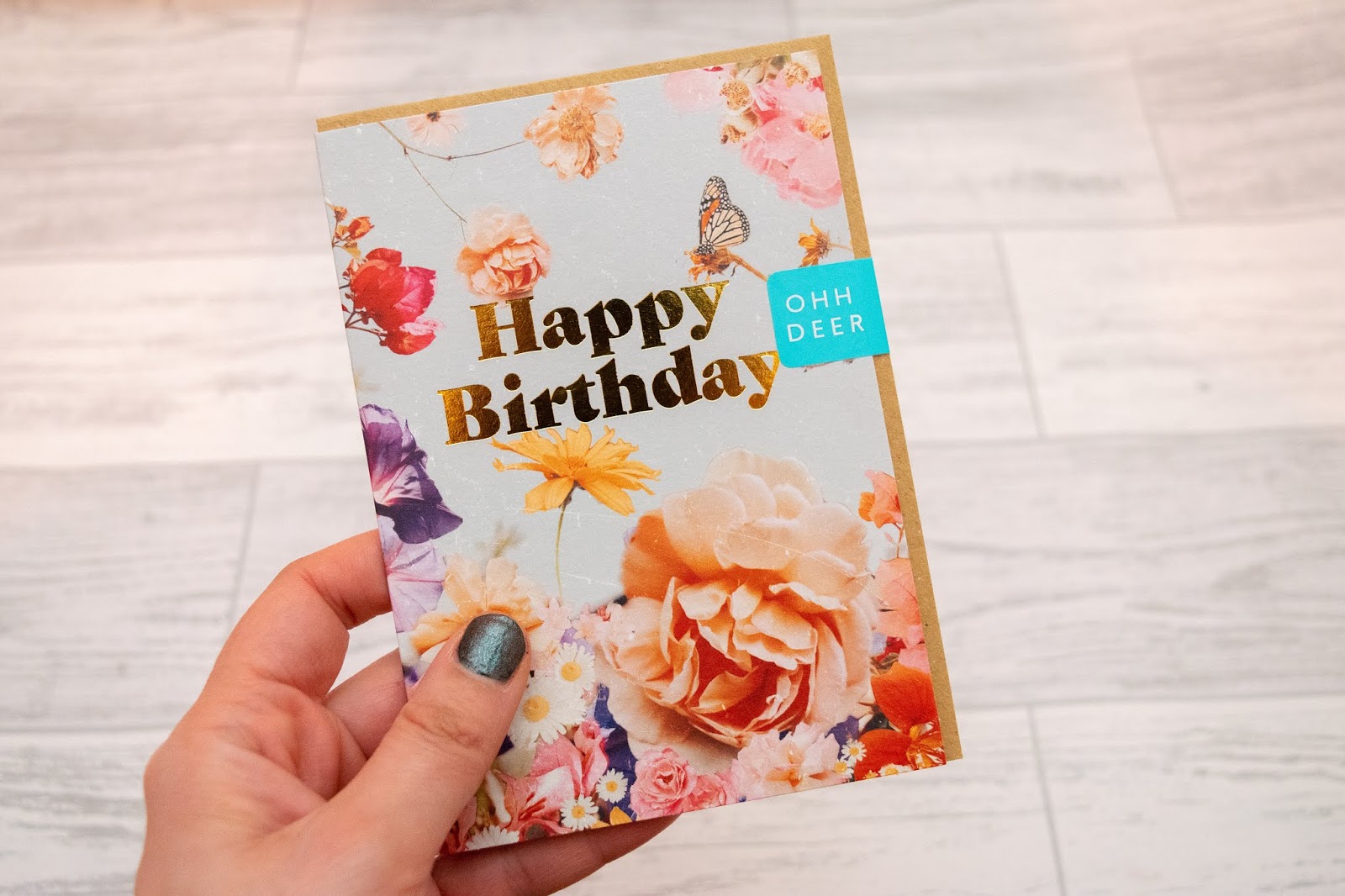 A small birthday card with happy birthday in gold foiling and a flowers on a light blue background.